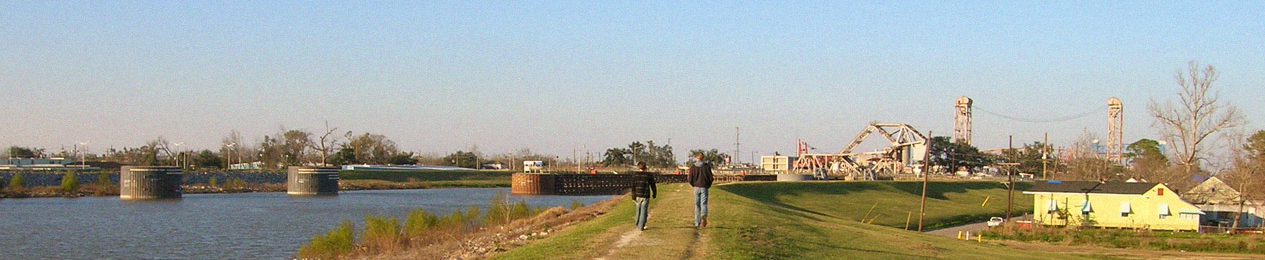 A photograph showing Post-K DuMarais and Timezone LaFontaine walking away from the camera on top of a levee in New Orleans next to the Mississippi River